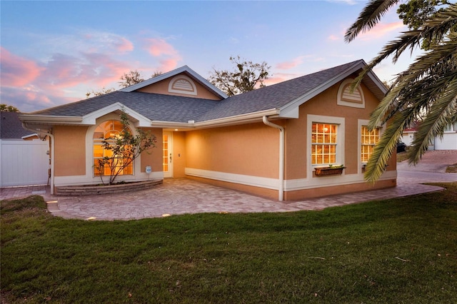 back of property featuring roof with shingles, fence, a lawn, and stucco siding