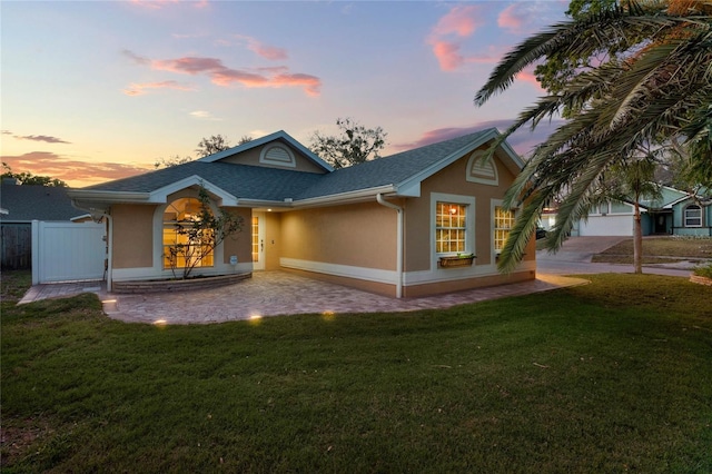 rear view of house featuring driveway, a lawn, roof with shingles, fence, and stucco siding