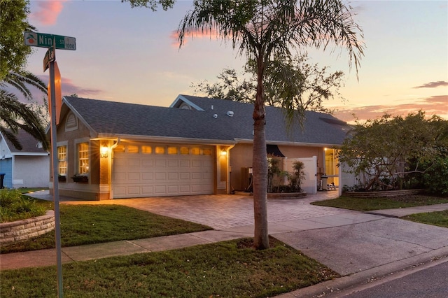 single story home with roof with shingles, decorative driveway, an attached garage, and stucco siding