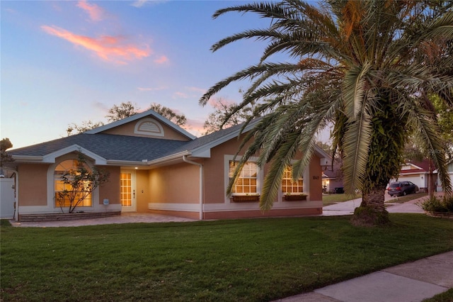 ranch-style home featuring roof with shingles, a front lawn, and stucco siding