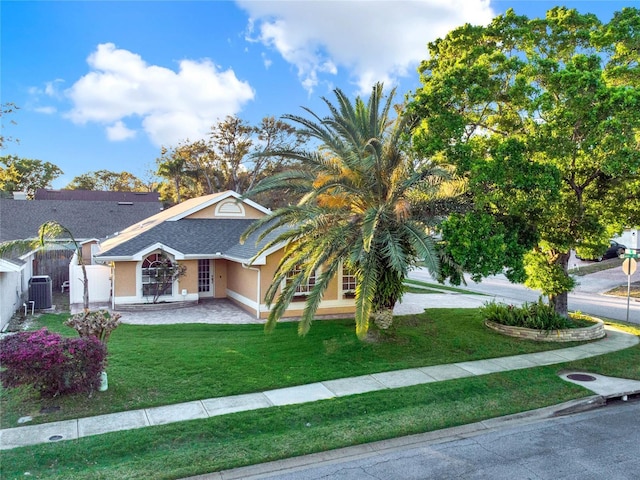 view of front facade featuring roof with shingles, stucco siding, central air condition unit, fence, and a front lawn