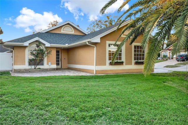 view of front of house with a shingled roof, a front yard, fence, and stucco siding