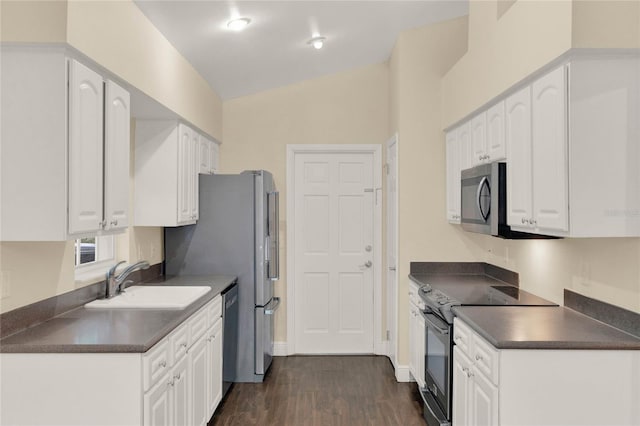 kitchen with stainless steel appliances, dark countertops, a sink, and white cabinetry