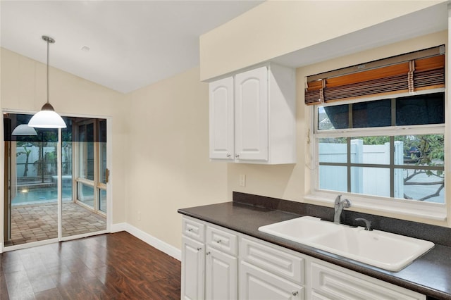 kitchen featuring dark countertops, white cabinets, a sink, and lofted ceiling