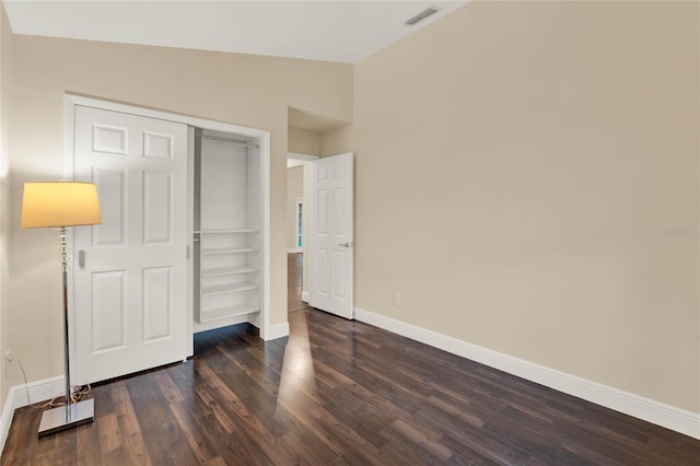 unfurnished bedroom with baseboards, visible vents, lofted ceiling, dark wood-style flooring, and a closet