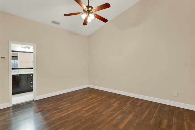 empty room featuring lofted ceiling, dark wood-type flooring, a ceiling fan, visible vents, and baseboards