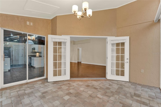 interior space with brick floor, french doors, a notable chandelier, and a textured wall