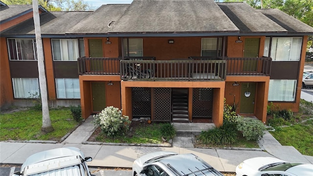 view of front of house featuring stucco siding, stairway, and roof with shingles