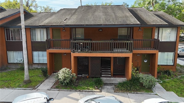 view of front facade featuring stucco siding, stairs, and roof with shingles