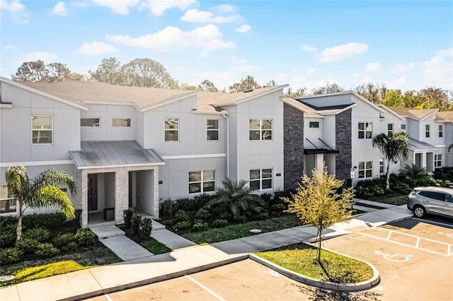 multi unit property featuring a residential view, metal roof, a standing seam roof, uncovered parking, and stucco siding