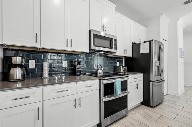 kitchen featuring tasteful backsplash, visible vents, appliances with stainless steel finishes, ornamental molding, and white cabinets