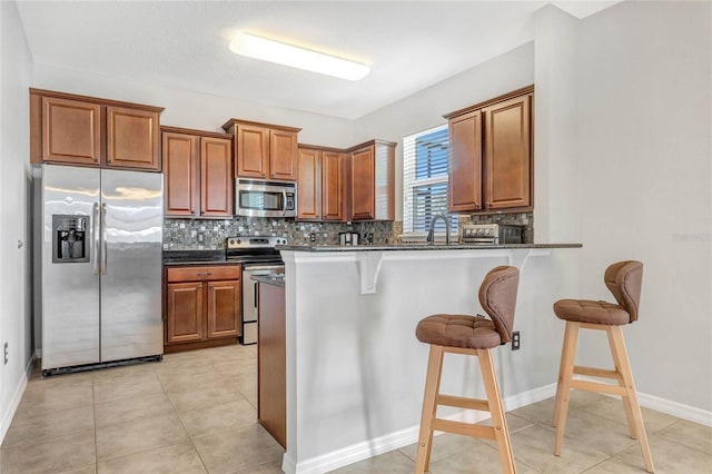 kitchen with decorative backsplash, a kitchen breakfast bar, brown cabinets, and appliances with stainless steel finishes