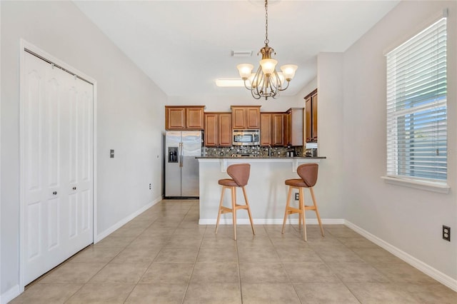 kitchen with tasteful backsplash, brown cabinets, a peninsula, hanging light fixtures, and stainless steel appliances