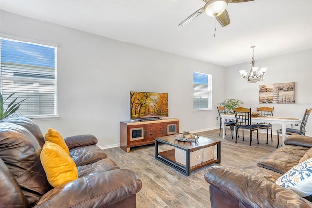 living room with light wood-type flooring, baseboards, and ceiling fan with notable chandelier