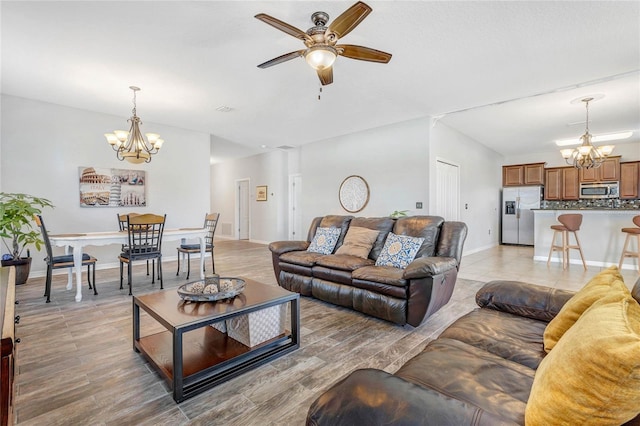 living room featuring ceiling fan with notable chandelier, baseboards, and light wood finished floors