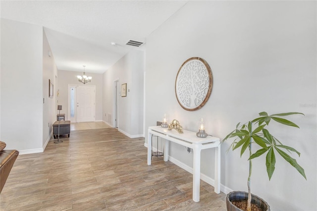 hall featuring baseboards, visible vents, light wood finished floors, and a chandelier