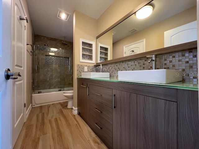 full bathroom featuring double vanity, backsplash, a sink, a combined bath / shower with rainfall shower, and wood finished floors