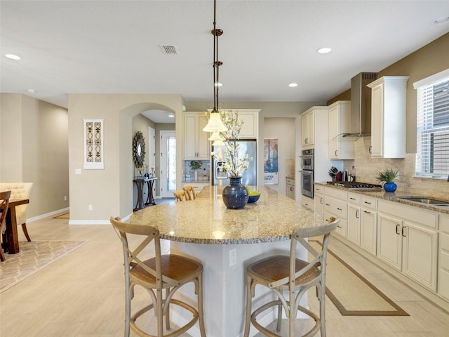 kitchen featuring visible vents, arched walkways, appliances with stainless steel finishes, wall chimney range hood, and a sink