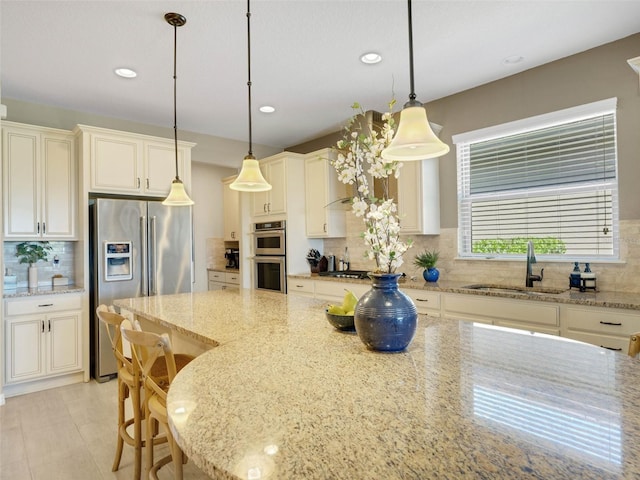 kitchen featuring light stone counters, a sink, appliances with stainless steel finishes, decorative backsplash, and decorative light fixtures