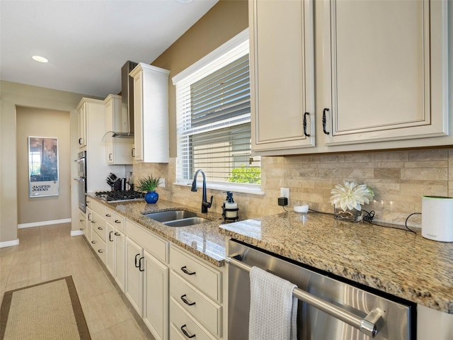 kitchen with light stone counters, backsplash, appliances with stainless steel finishes, a sink, and baseboards