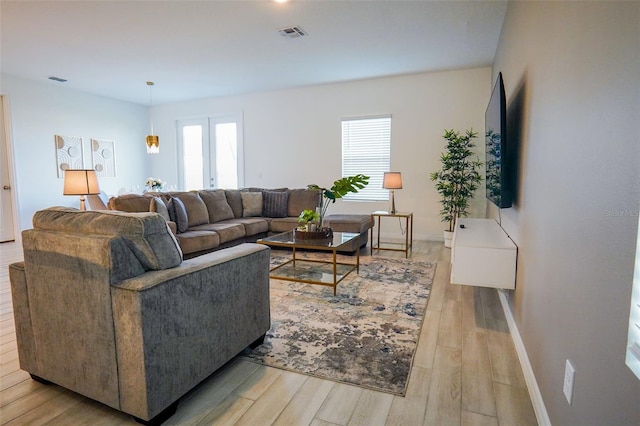 living room featuring baseboards, plenty of natural light, visible vents, and light wood-style floors