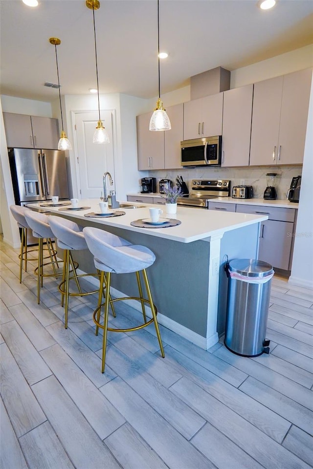 kitchen with gray cabinetry, wood finish floors, appliances with stainless steel finishes, tasteful backsplash, and a kitchen bar