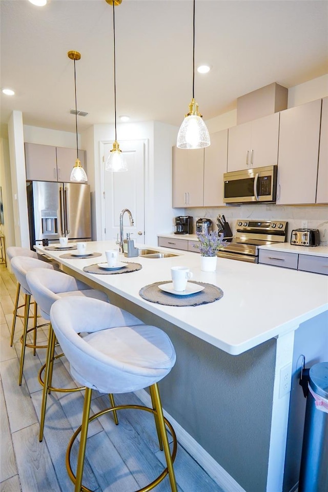 kitchen featuring appliances with stainless steel finishes, light countertops, a sink, and light wood finished floors