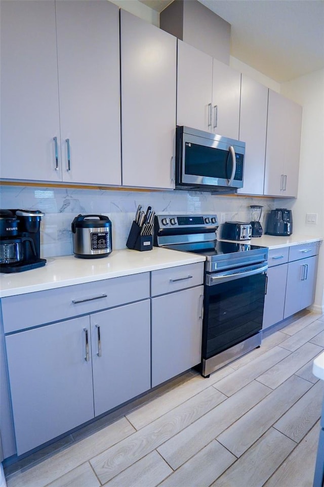 kitchen featuring appliances with stainless steel finishes, decorative backsplash, light countertops, and wood finish floors