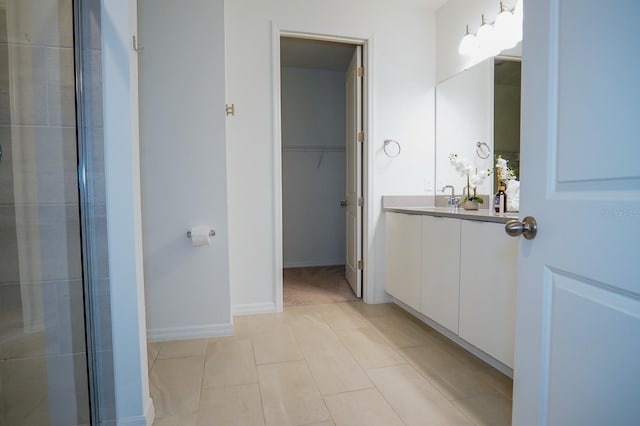 full bath featuring tile patterned flooring, vanity, baseboards, a spacious closet, and a tile shower