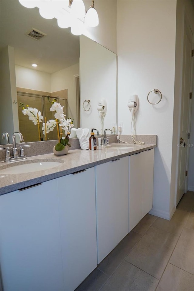 bathroom with double vanity, a stall shower, a sink, and visible vents