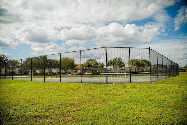 view of tennis court with fence and a yard