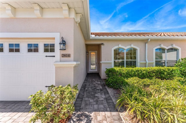 view of exterior entry with a tile roof, a garage, and stucco siding