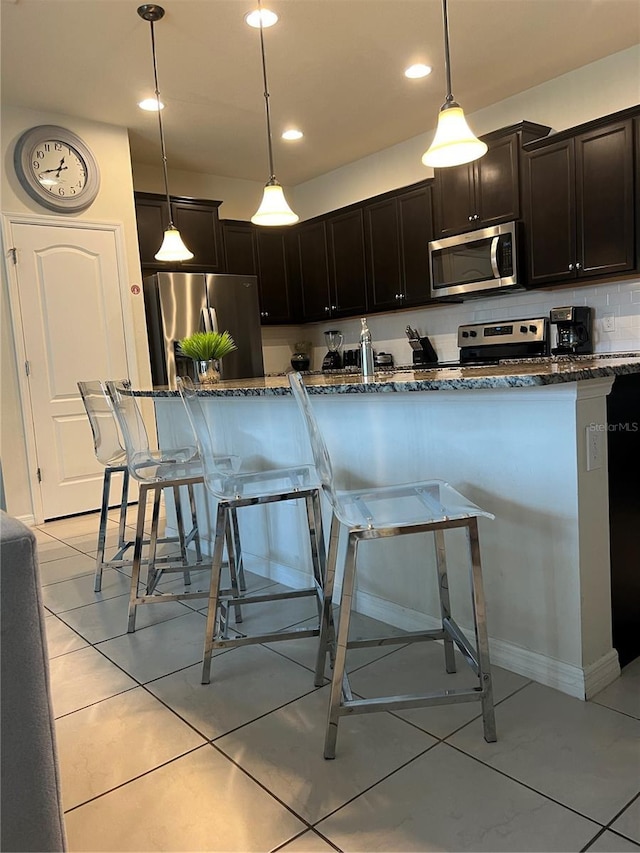 kitchen with dark stone counters, stainless steel appliances, a breakfast bar area, and backsplash