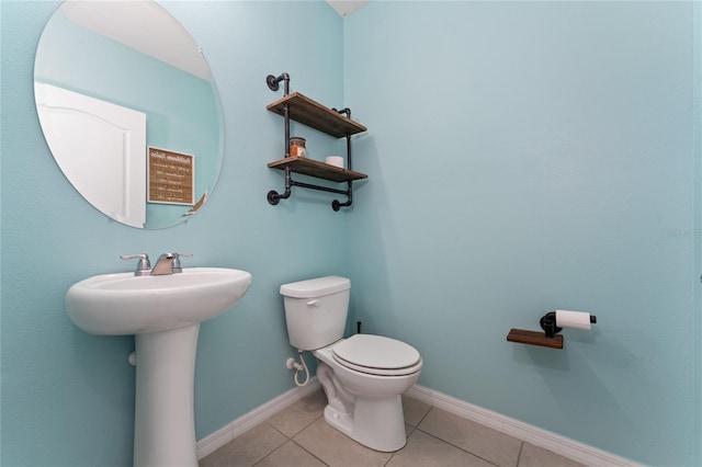 half bath featuring a sink, tile patterned flooring, toilet, and baseboards