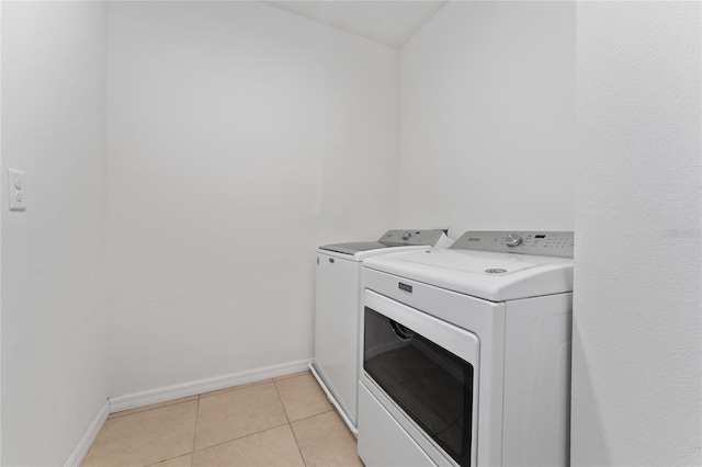 clothes washing area featuring light tile patterned floors, laundry area, independent washer and dryer, and baseboards