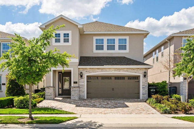 view of front facade featuring a garage, stone siding, decorative driveway, and stucco siding