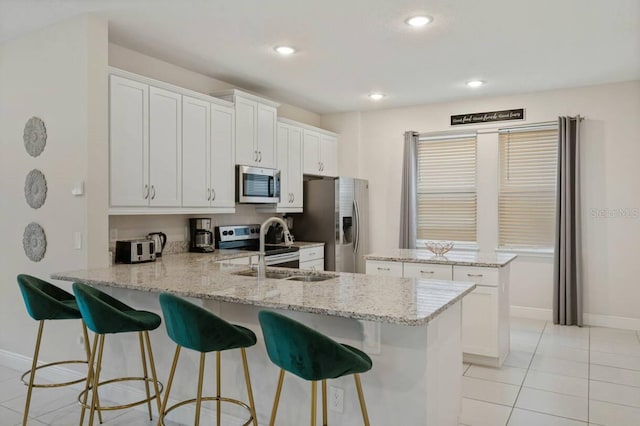 kitchen with a kitchen island, light stone counters, a peninsula, stainless steel appliances, and a sink