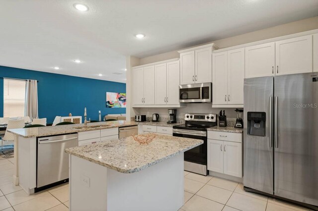 kitchen featuring white cabinets, a kitchen island, a peninsula, stainless steel appliances, and a sink