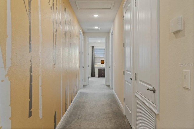 hallway featuring attic access, visible vents, baseboards, and carpet flooring