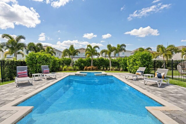 view of swimming pool featuring a pool with connected hot tub, fence, and a patio