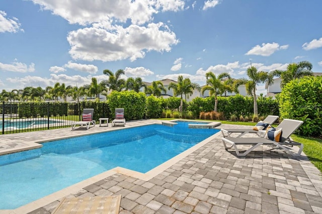 view of swimming pool featuring a pool with connected hot tub, fence, and a patio