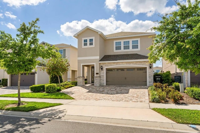 view of front facade with a garage, a shingled roof, stone siding, decorative driveway, and stucco siding