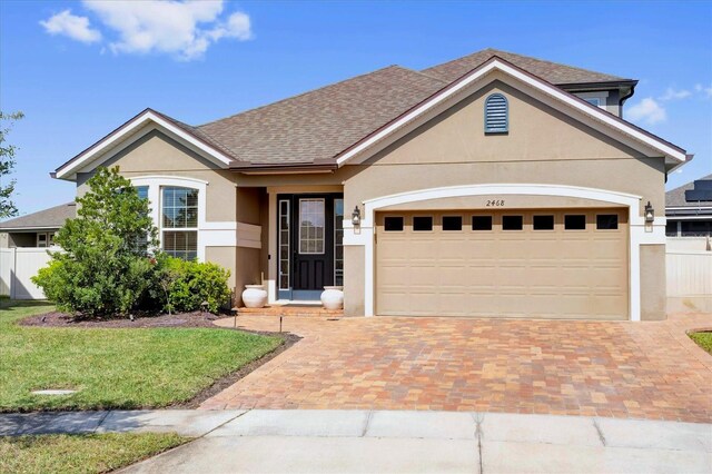 ranch-style house featuring stucco siding, decorative driveway, fence, an attached garage, and a shingled roof