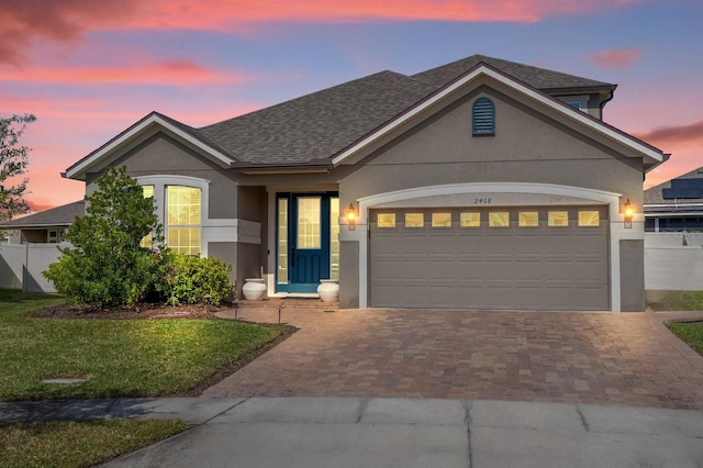 view of front facade featuring stucco siding, decorative driveway, fence, a shingled roof, and a garage