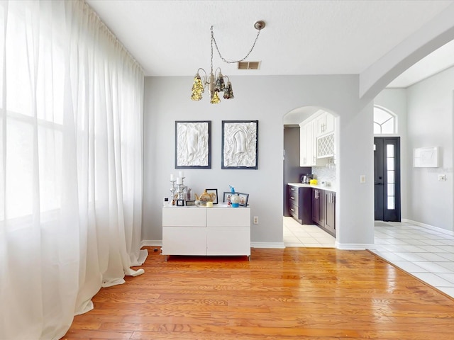 1718 Golfview Dr, Kissimmee, FL 34746 - unfurnished dining area featuring visible vents, arched walkways, baseboards, light wood-style flooring, and an inviting chandelier