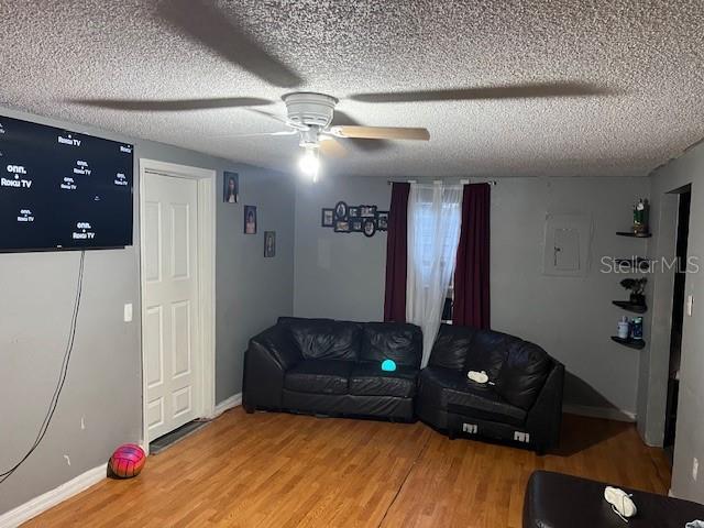 living area with baseboards, a textured ceiling, light wood-style floors, and a ceiling fan