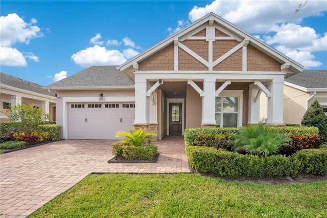 craftsman inspired home with a garage, roof with shingles, decorative driveway, and stucco siding