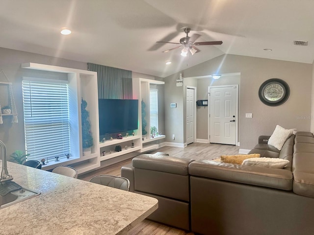 living area with visible vents, light wood-style flooring, baseboards, lofted ceiling, and ceiling fan