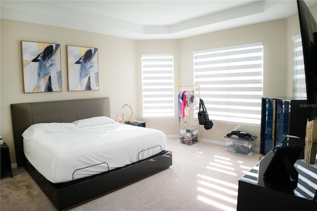 carpeted bedroom with a tray ceiling and baseboards