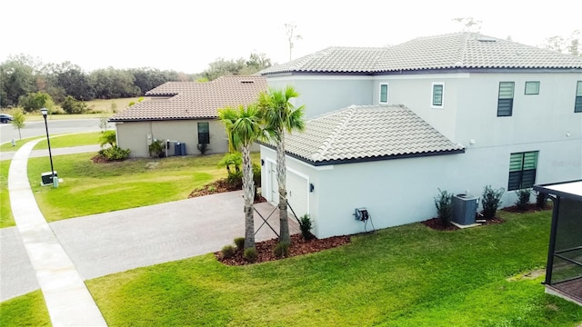 back of house with a tile roof, stucco siding, concrete driveway, a lawn, and central AC